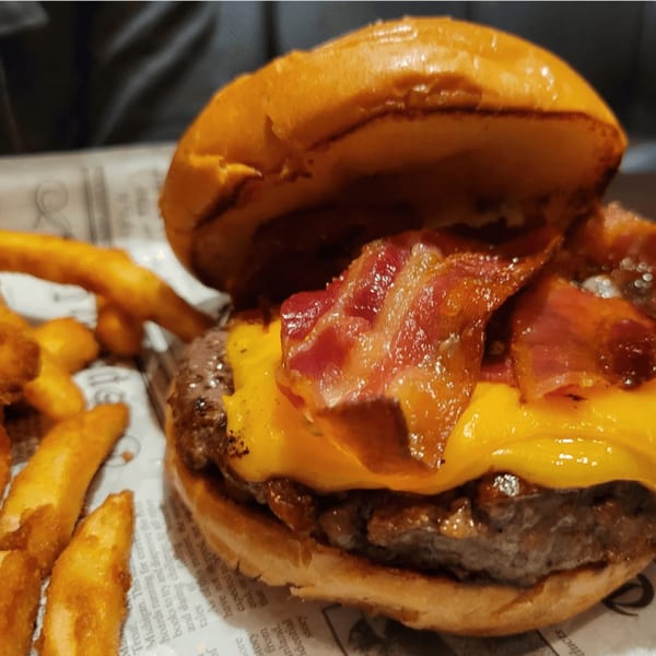 Close-up of a bacon cheeseburger with fries on a newspaper-lined tray.