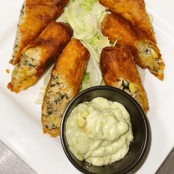 Golden-brown fried spring rolls with a savory filling, served with shredded lettuce and a creamy green dipping sauce.