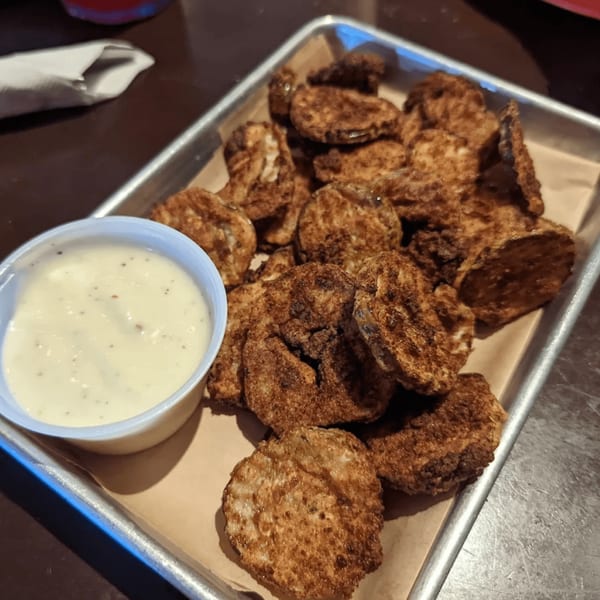 A metal tray filled with crispy fried pickles and a side of creamy dipping sauce.