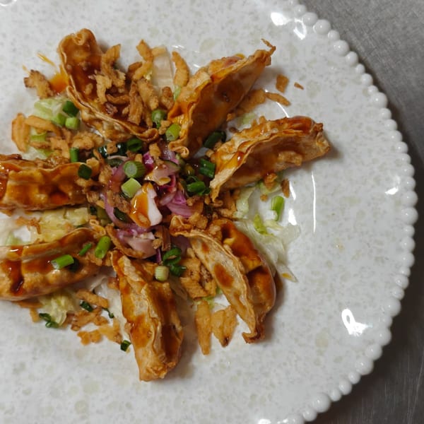 Fried dumplings drizzled with sauce, topped with crispy onions, green onions, and red onions.
