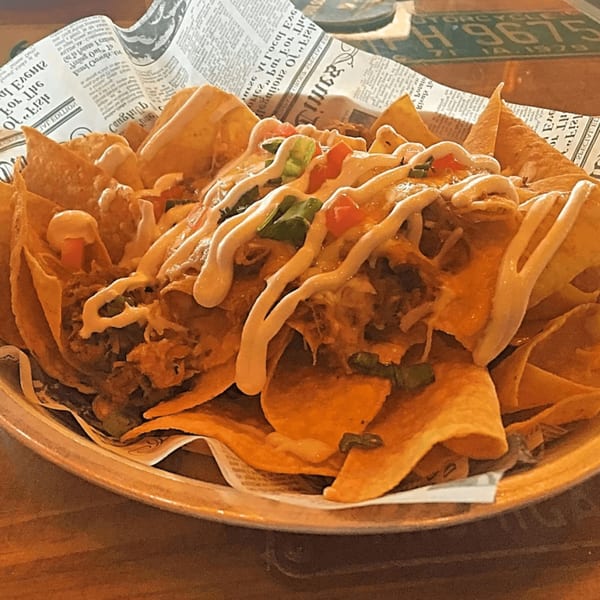 A large plate of loaded nachos with cheese, meat, and toppings, served on newspaper-print paper.