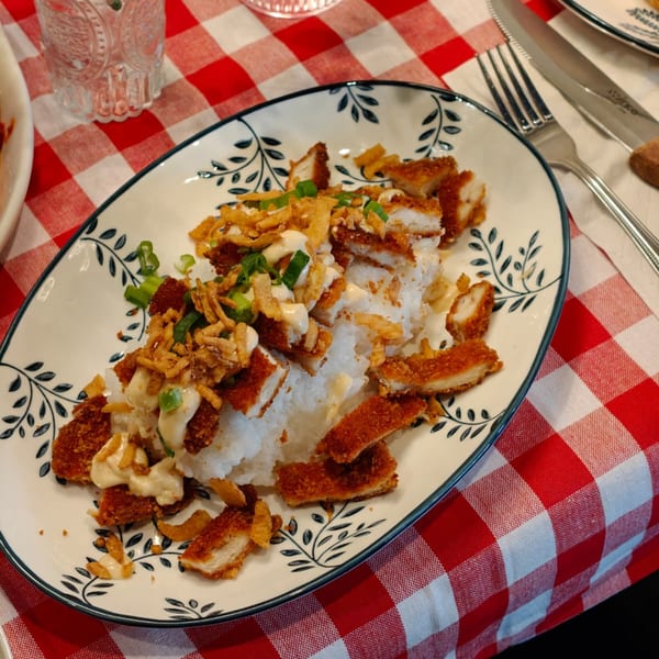 Crispy fried chicken pieces with rice, creamy sauce, and green onions on a decorative plate.